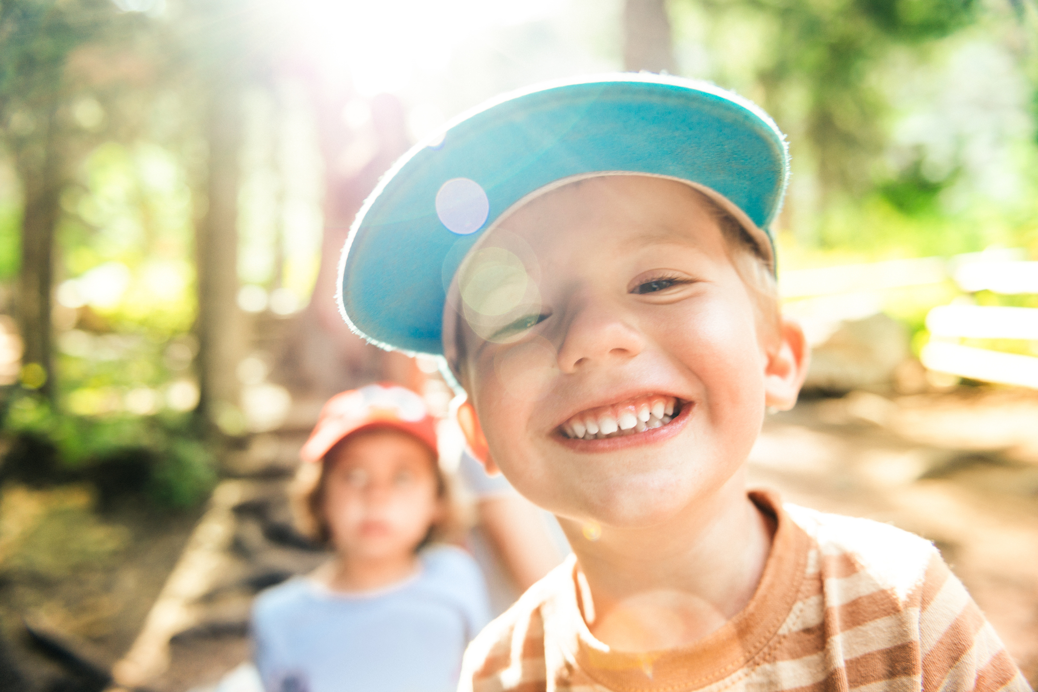 A boy wearing a hat is smiling in the woods.